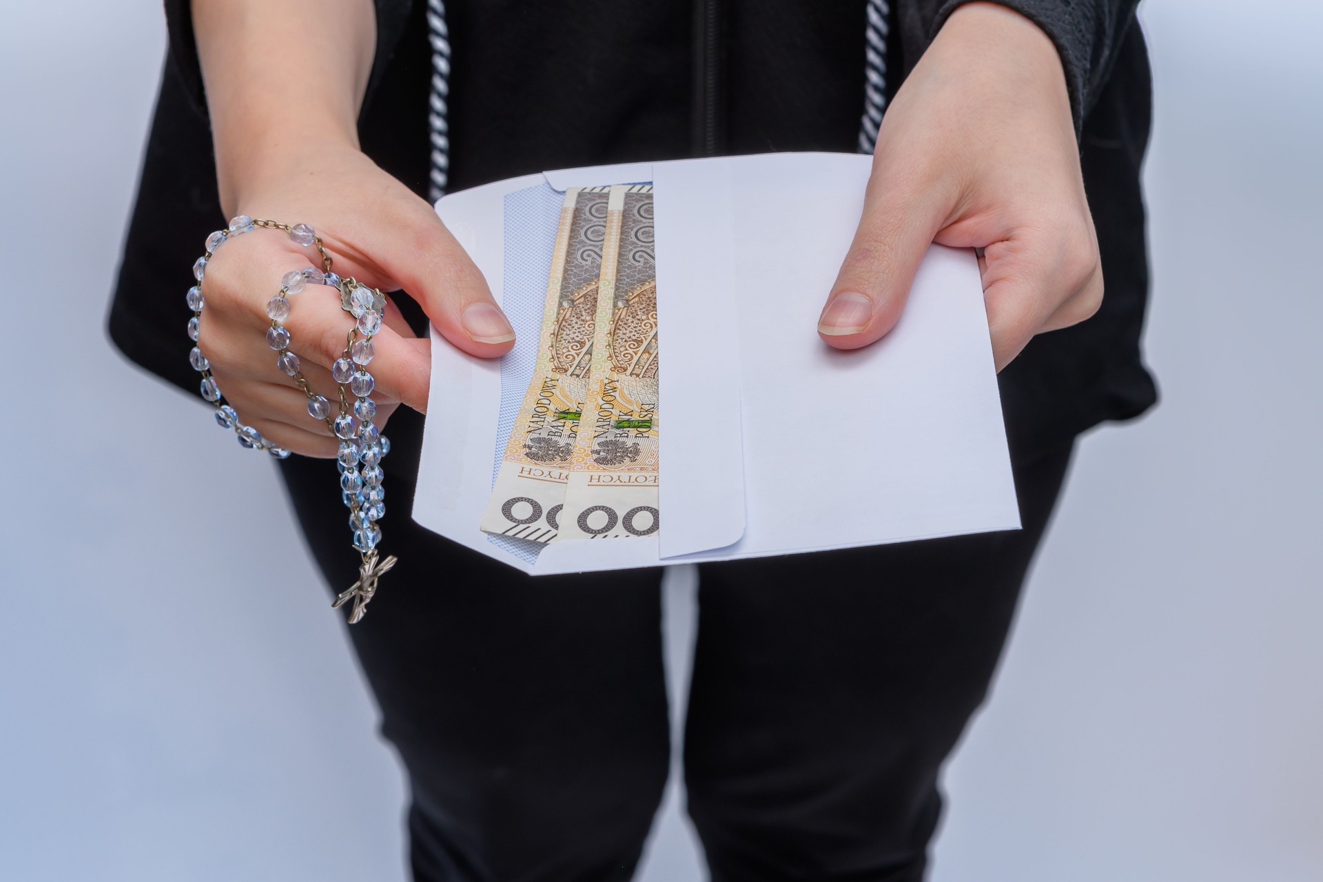 The woman holds an envelope with Polish money and a rosary in her hands